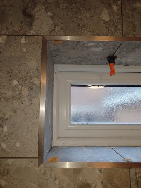 Tiled window reveal finished with a brushed metal edge trim